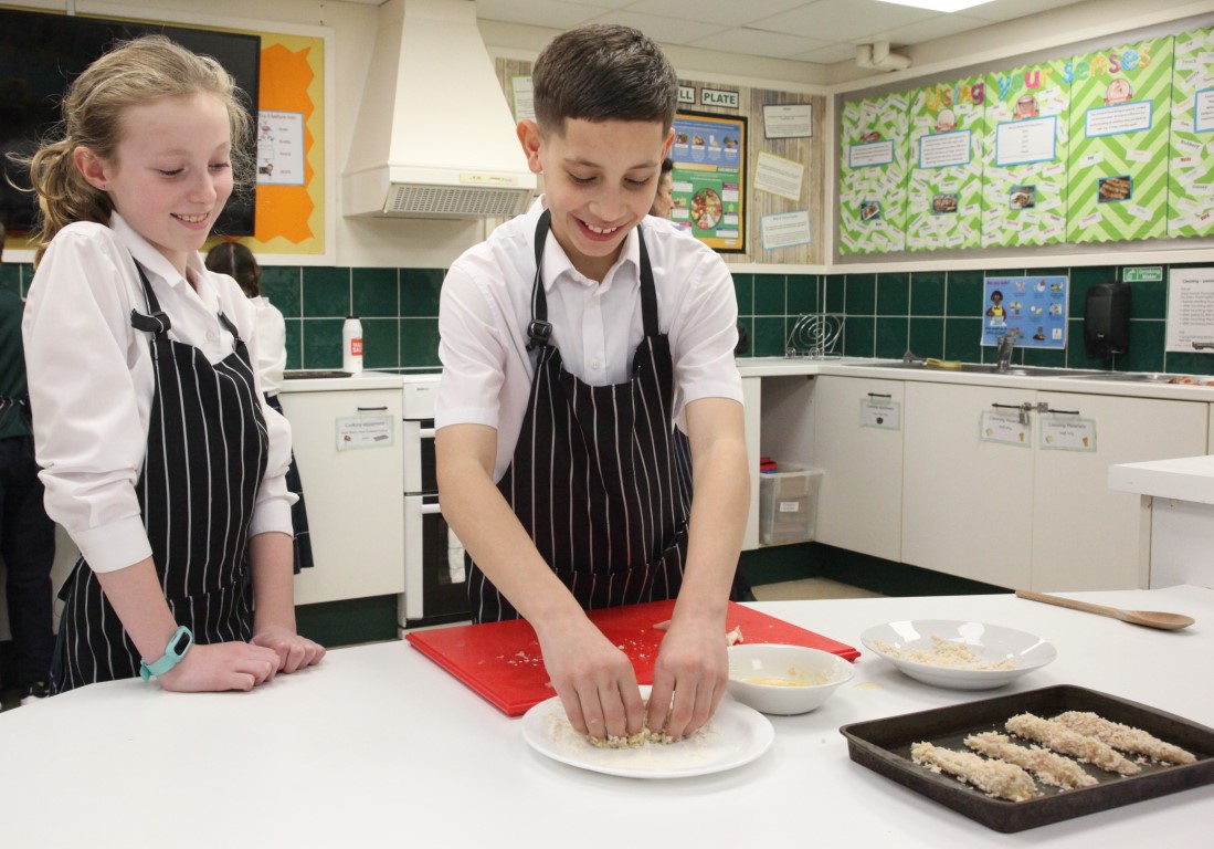 A Year 6 boy prepares breaded chicken fillets in the food tech kitchen