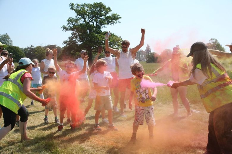 children and grown ups being sprayed in bright paint colours during the school charity colour run