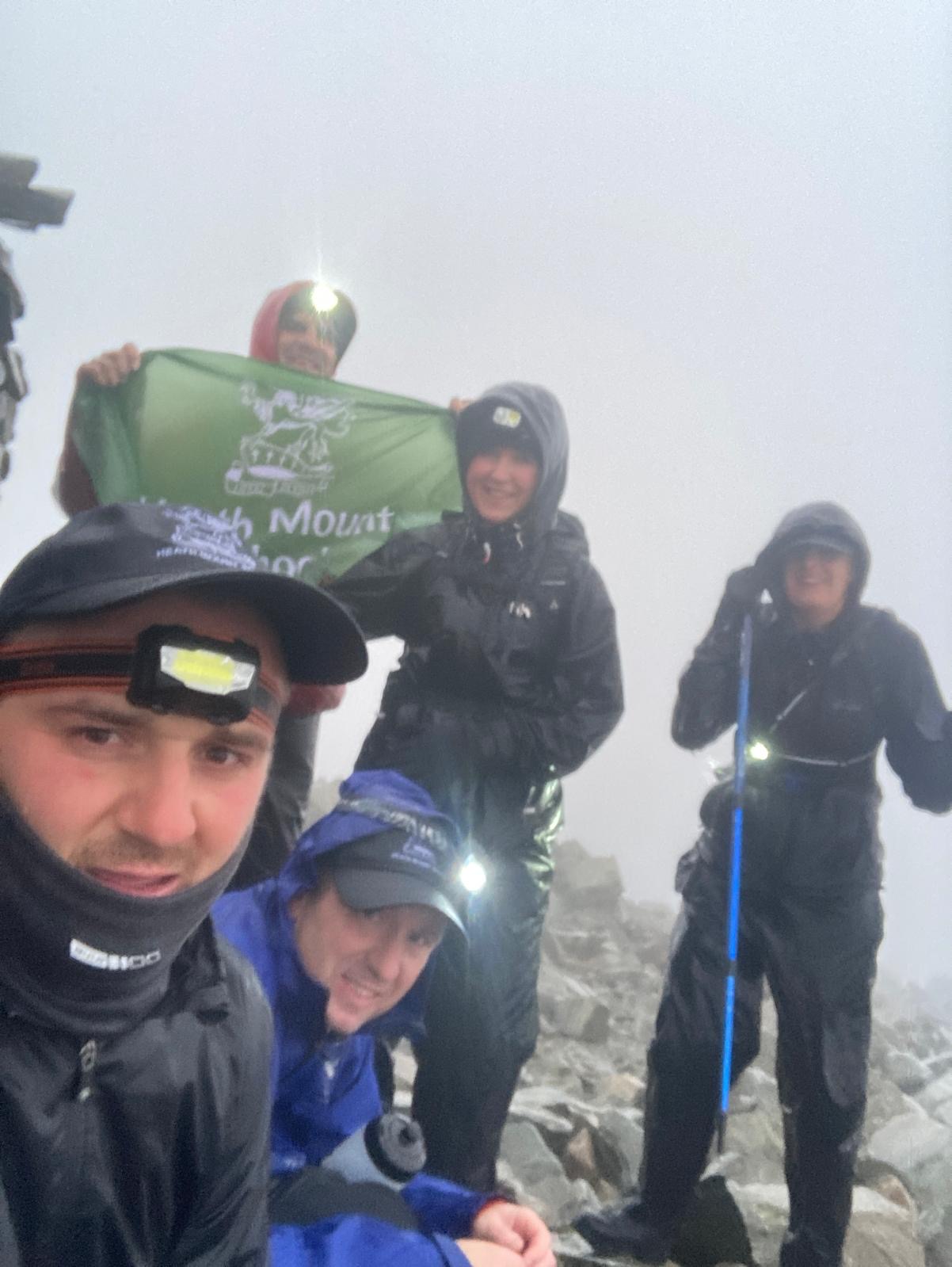 Scafell Pike Summit 6 staff members pose with a flag at the top of Scafell Pike