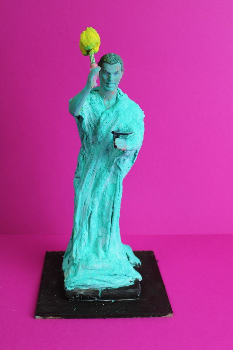 a Ken barbie doll wrapped in green with a candle to imitate the statue of liberty