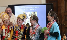 Four children dress in royal robes laugh as they take part in  a workshop with a Buddhist monk