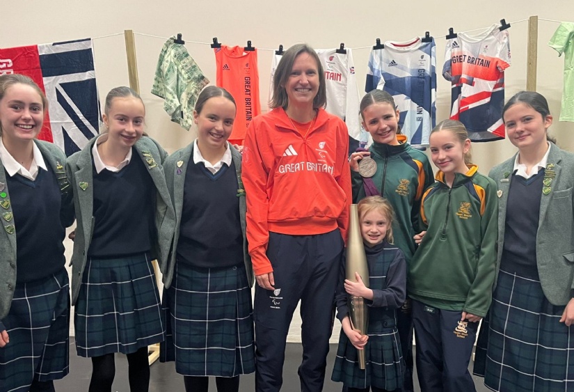 Verity Naylor poses with students holding a London 2012 Paralympic Silver Medal and a Paris 2024 Paralympic Torch